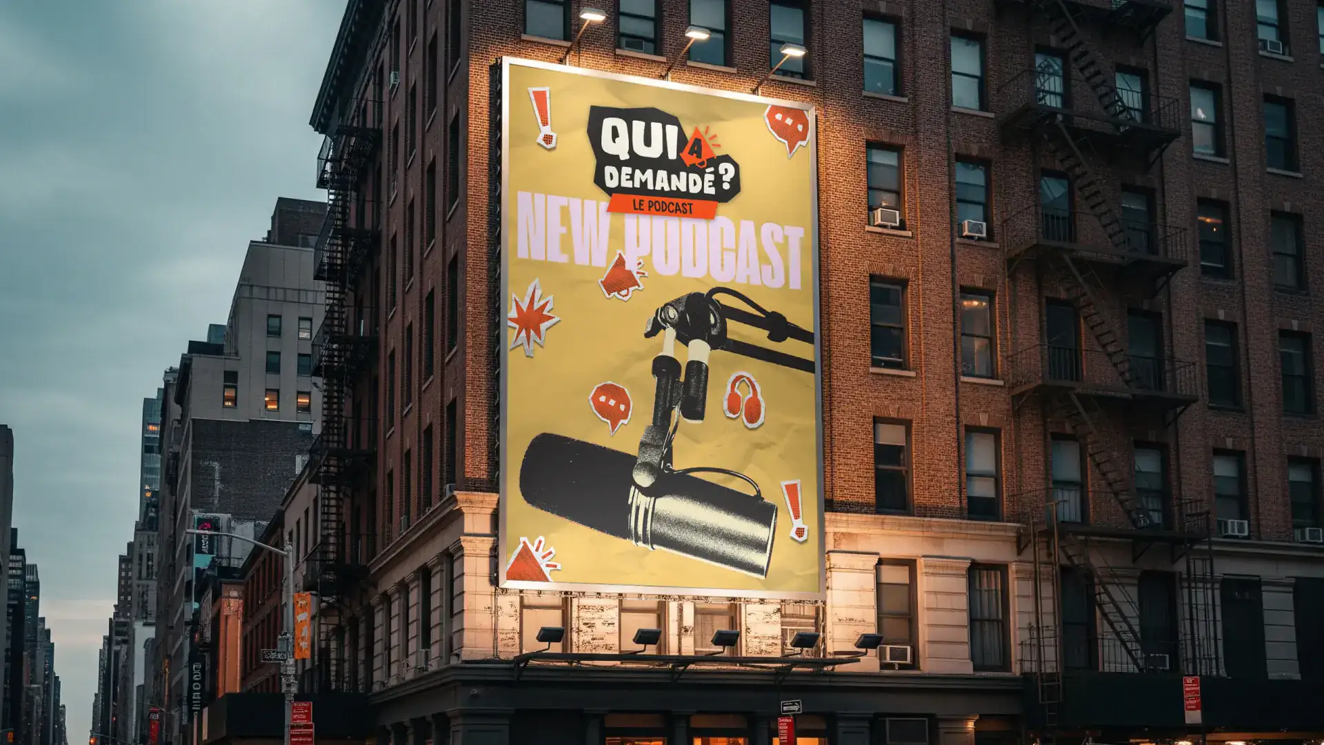 Affiche géante Qui a demandé ? sur la façade d’un immeuble en brique, fond jaune maïs, micro de studio et mention « new podcast ».